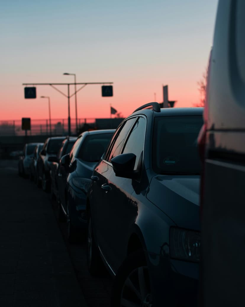 Silhouetted cars parked along a city street beneath a vibrant orange and pink sunset sky during golden hour.