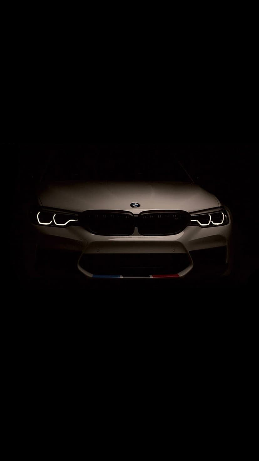 BMW M5 front end with glowing circular headlights and a white kidney grille against a pitch black background.
