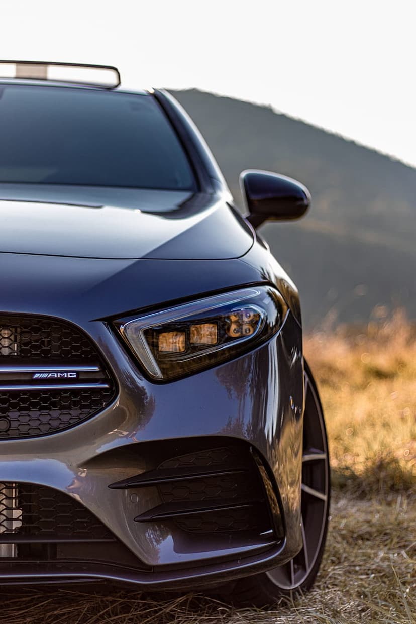 Mercedes-AMG front grille and LED headlight detail against a blurred hilly background in a vertical car shot.