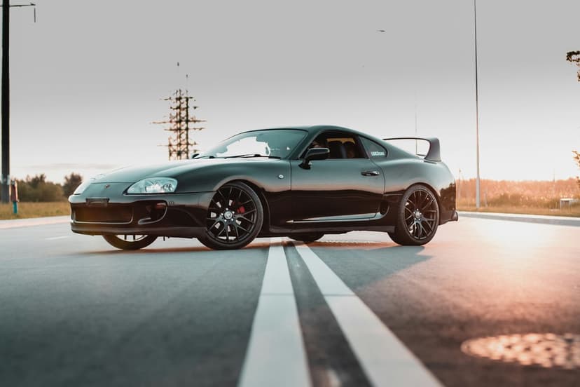 Black Toyota Supra Mk4 with red calipers on an empty road during a hazy sunset with golden hour lighting.