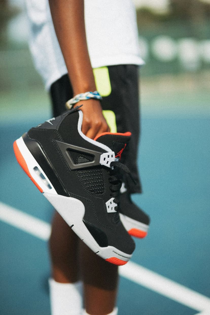 Black and red Air Jordan 4 sneakers held by a person's hand, showing detailed mesh and nubuck materials.