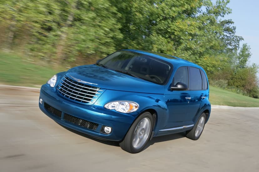 Blue Chrysler PT Cruiser driving on a road with motion blur against a background of lush green trees and sky.