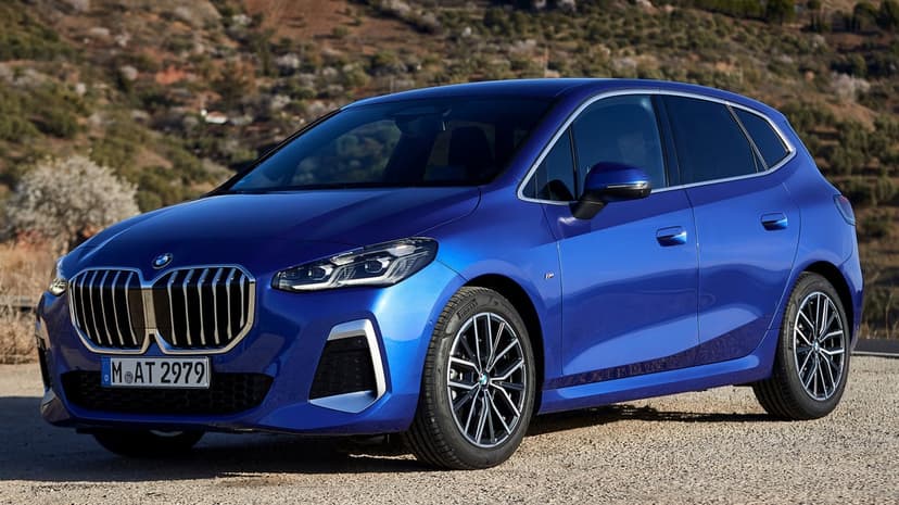 Deep metallic blue BMW car with chrome accents parked on a gravel path against a soft-focus hilly landscape.