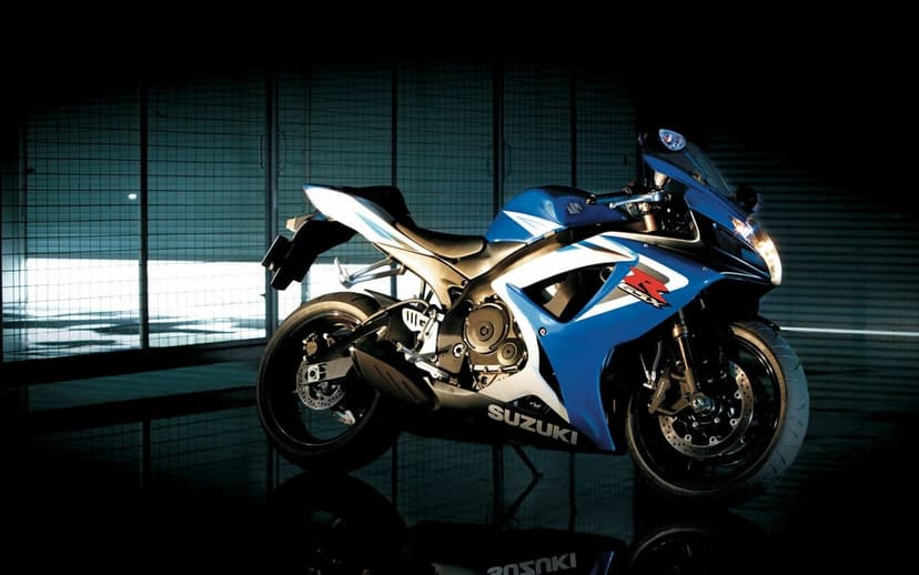 Blue Suzuki GSX-R sportbike parked on a reflective dark floor against an industrial metal grate background.