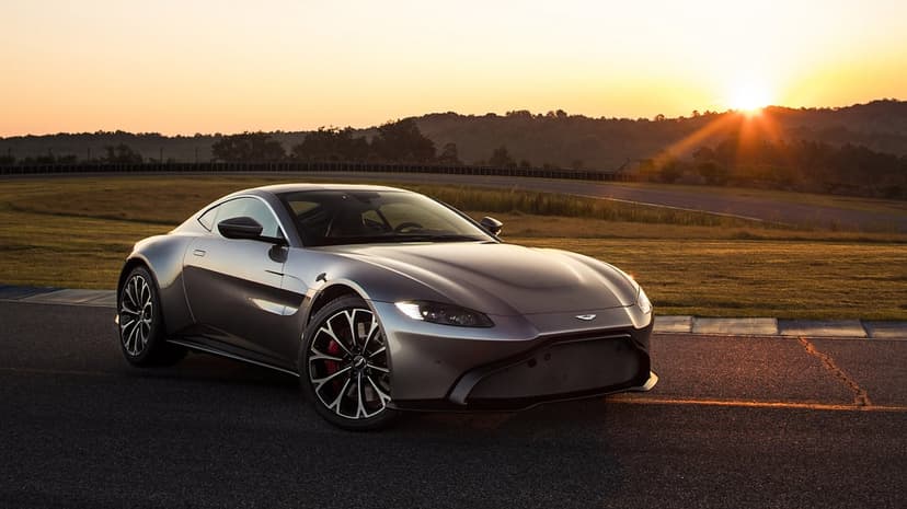 Silver Aston Martin Vantage on a race track at sunset with golden sunlight reflecting on its metallic body.