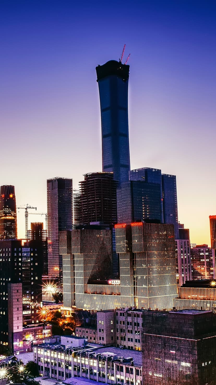 Beijing skyscrapers including the CCTV building glow with office lights under a blue and orange twilight sky.