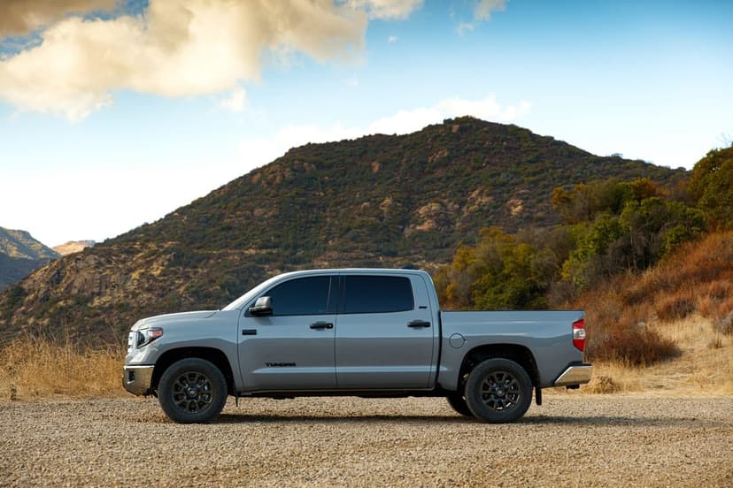 Gray Toyota Tundra parked on gravel with a large green mountain and golden clouds in the background.