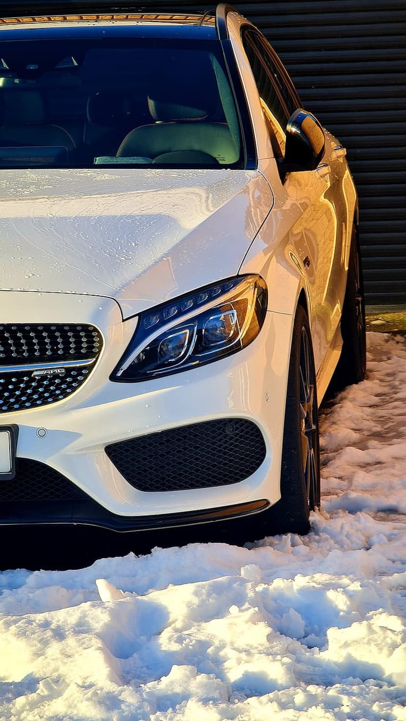 White Mercedes AMG SUV with snow on the front grille parked in a winter setting with LED headlights visible.