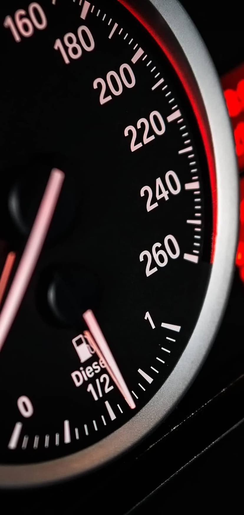 Speedometer with a glowing red needle and white numbers next to a diesel fuel gauge on a dark car dashboard.