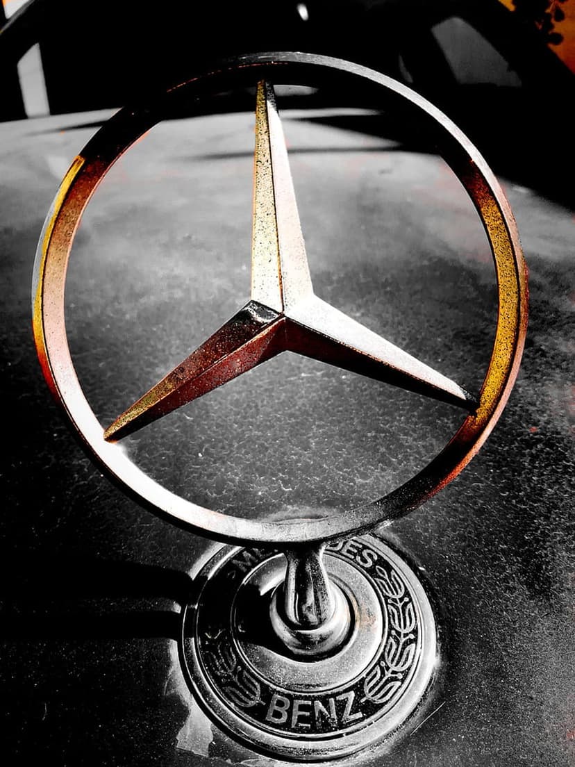 Mercedes-Benz three-pointed star logo with bronze patina and chrome trim mounted on a dark textured car hood.