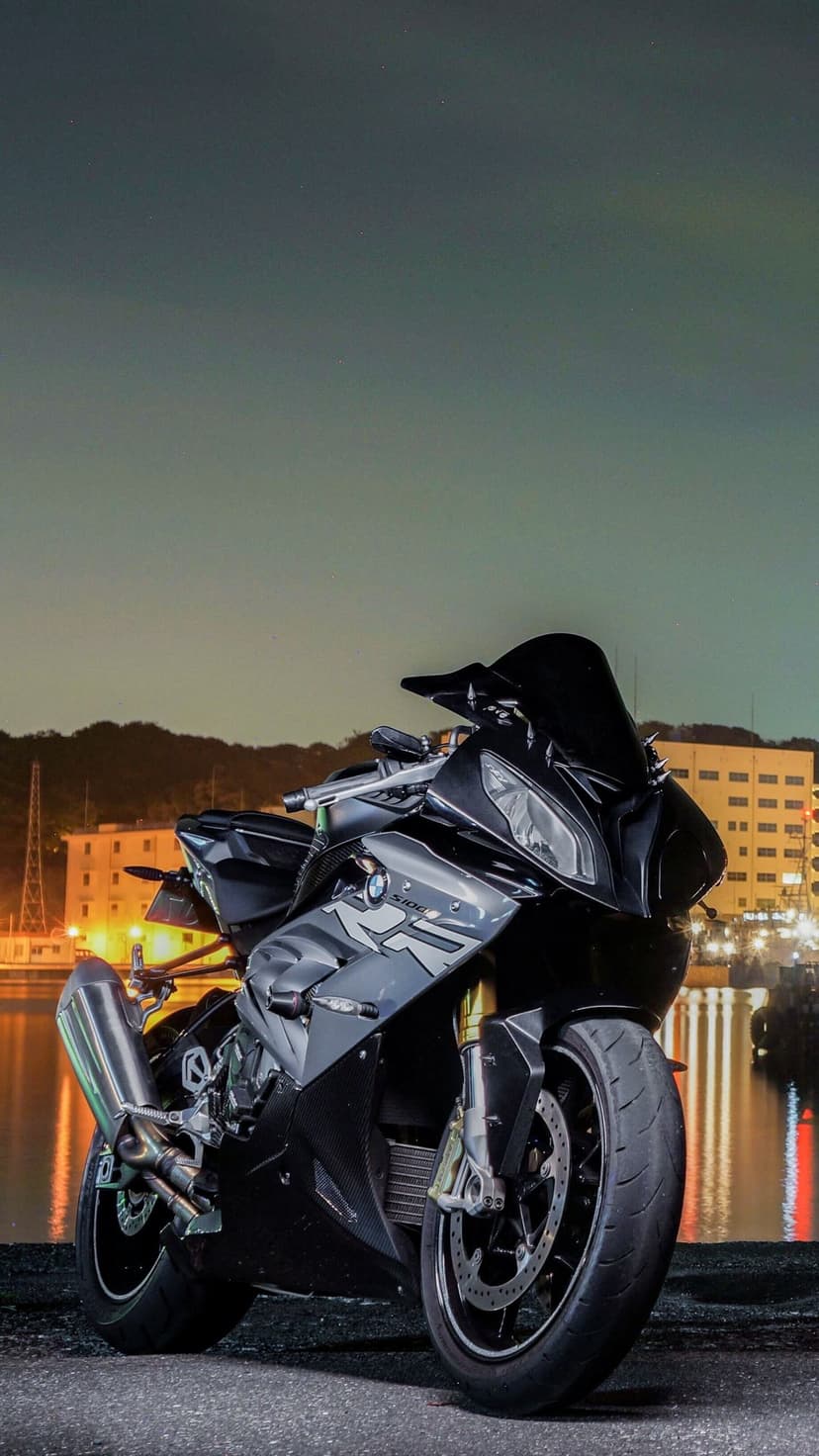 Black BMW S1000RR motorcycle parked on a dark pier with illuminated city buildings reflecting in the water.