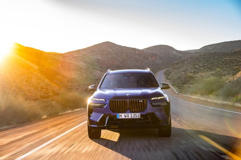 Purple luxury SUV driving on a desert mountain road during a golden sunset with a bright lens flare.