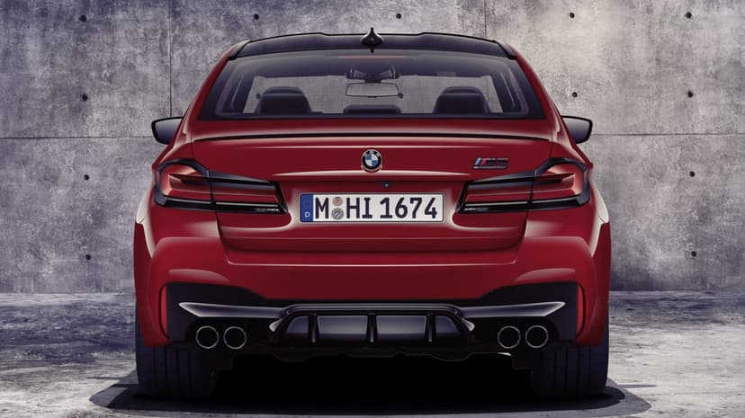 Rear view of a red BMW M5 Competition with quad exhausts and black diffuser against a gray concrete wall.
