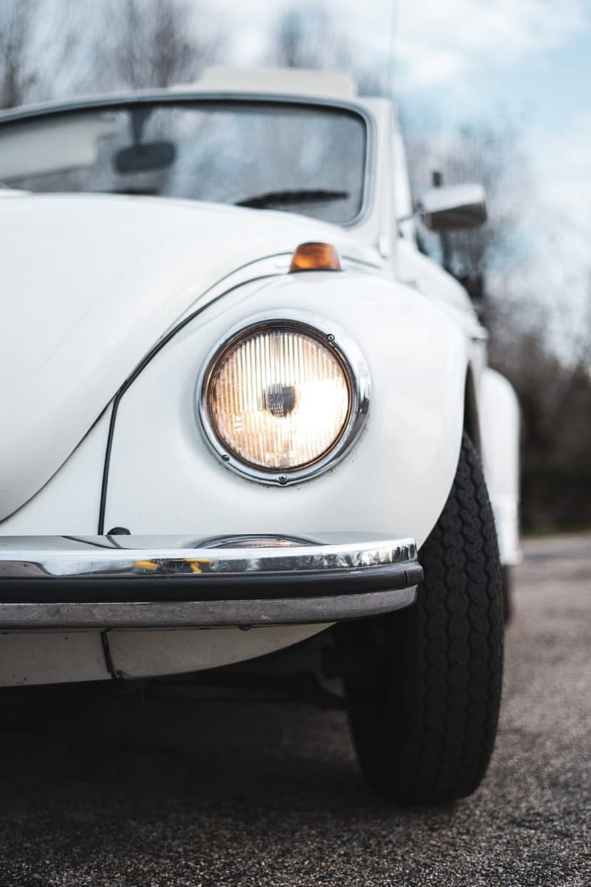 White vintage car headlight with chrome trim and an amber turn signal lens against a soft outdoor background.