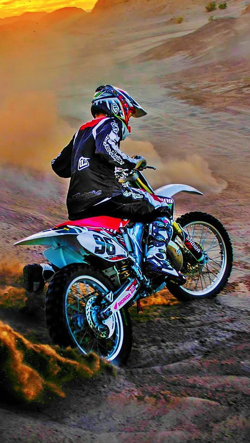 Motocross rider in full racing gear leans into a turn while kicking up a trail of golden dust during sunset.