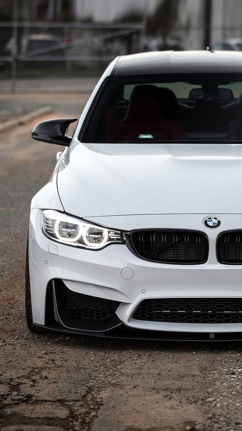 White BMW M4 Coupe front bumper with black kidney grilles and glowing LED headlights in a vertical close-up.