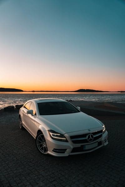 White Mercedes CLS on cobblestone beach at sunset