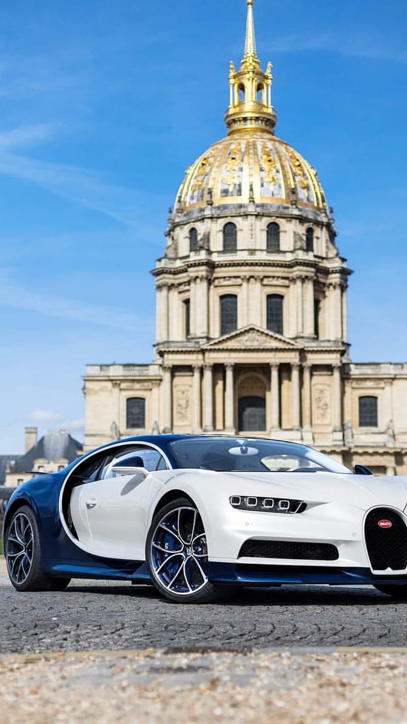 White and blue Bugatti Chiron parked on a Paris street with the golden dome of Les Invalides in the background.