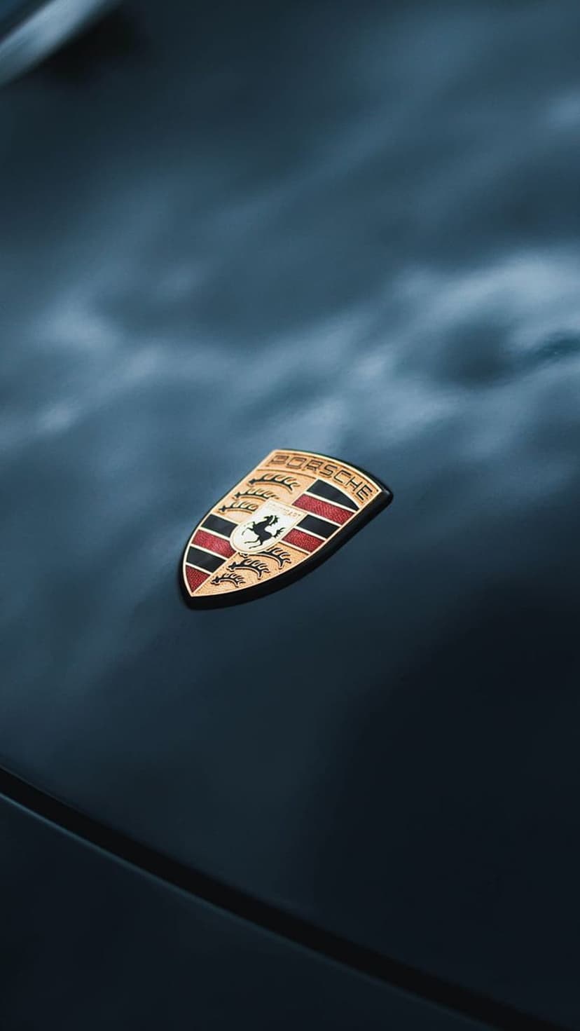 Porsche gold shield emblem with red stripes and horse icon centered on a reflective black metallic surface.