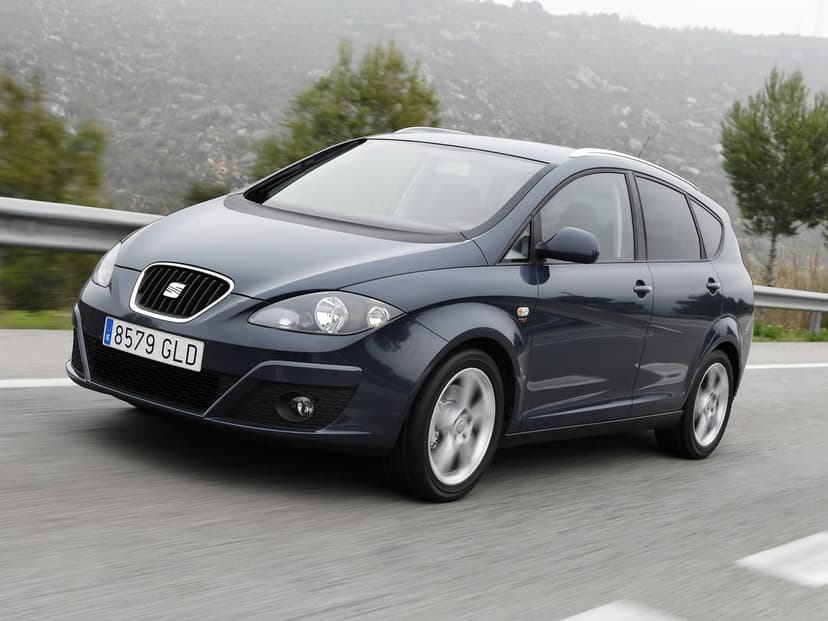 Dark blue SEAT Altea XL driving on a winding mountain road under a hazy, overcast sky with motion-blurred wheels.