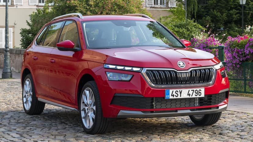 Red Skoda Kamiq SUV parked on a grey cobblestone street with purple flowers and green trees in the background.