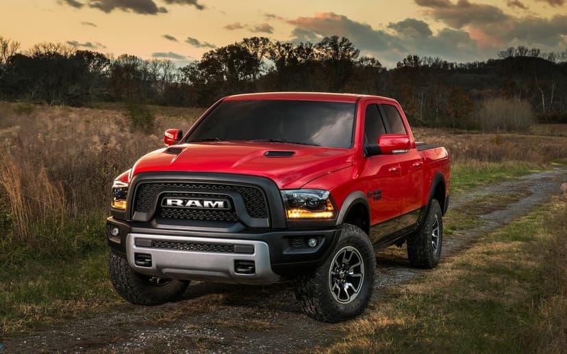 Red Ram 1500 Rebel truck with amber lights on a dirt path in a rural field at sunset under a cloudy sky.