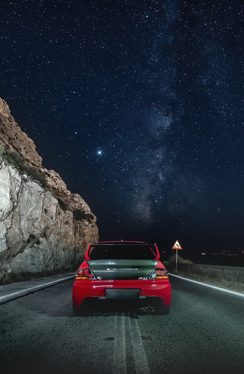 Red Mitsubishi Lancer Evolution rear view on a mountain road under a starry Milky Way galaxy night sky.