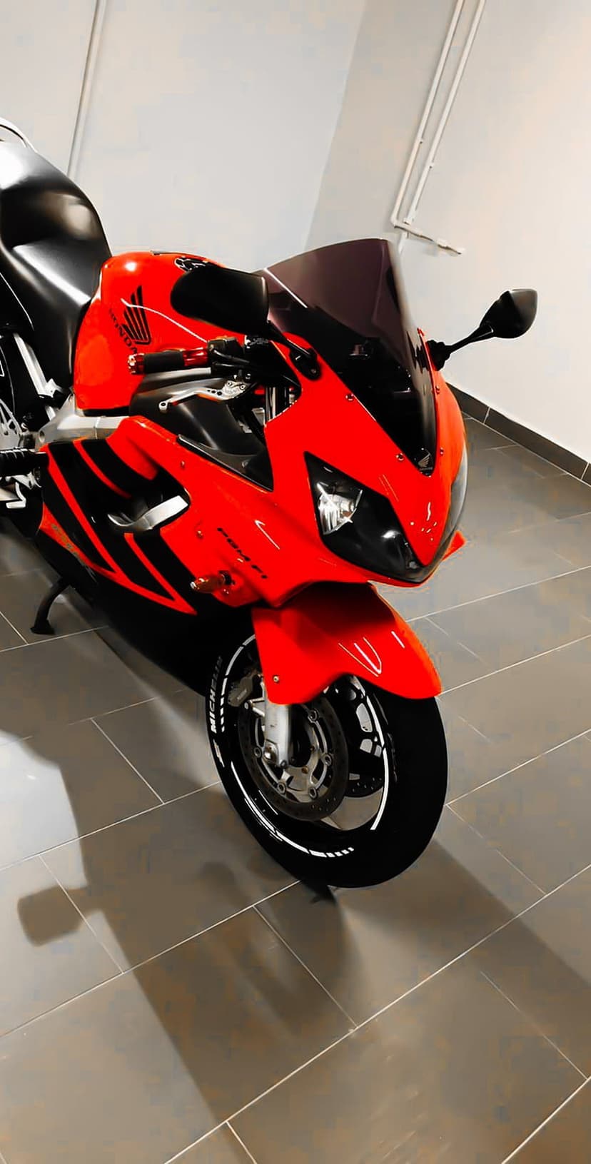 Red Honda CBR motorcycle parked on a tiled garage floor with visible reflections and sharp black accents.