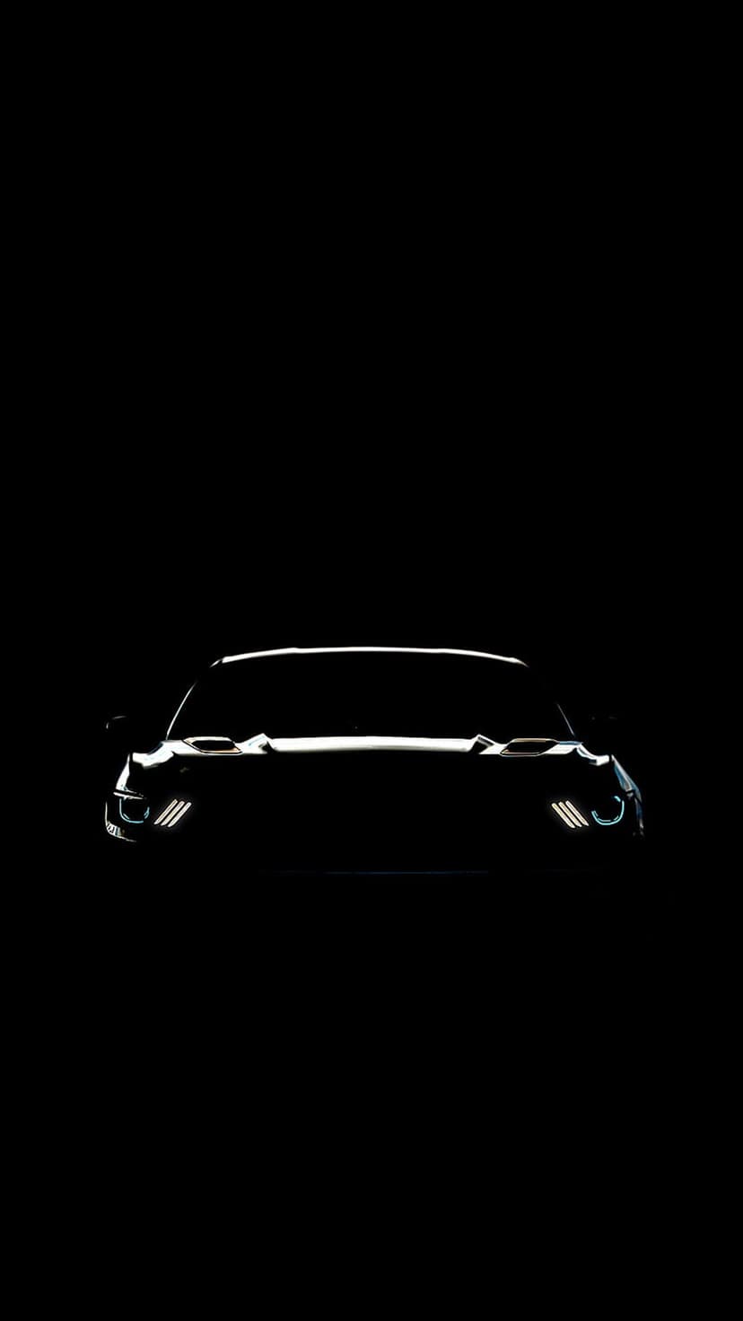 Ford Mustang LED headlights glow with triple-bar signature lights against a dark black silhouetted car front.