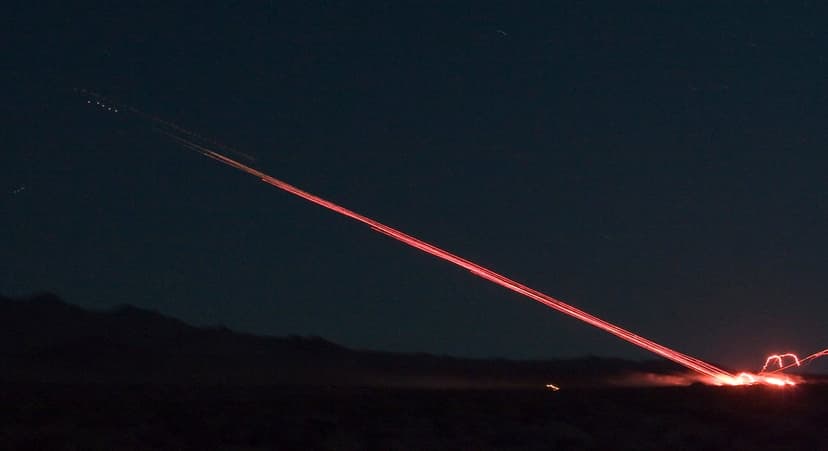 Fiery red rocket trail arcing across a dark night sky above silhouetted desert mountains and distant stars.