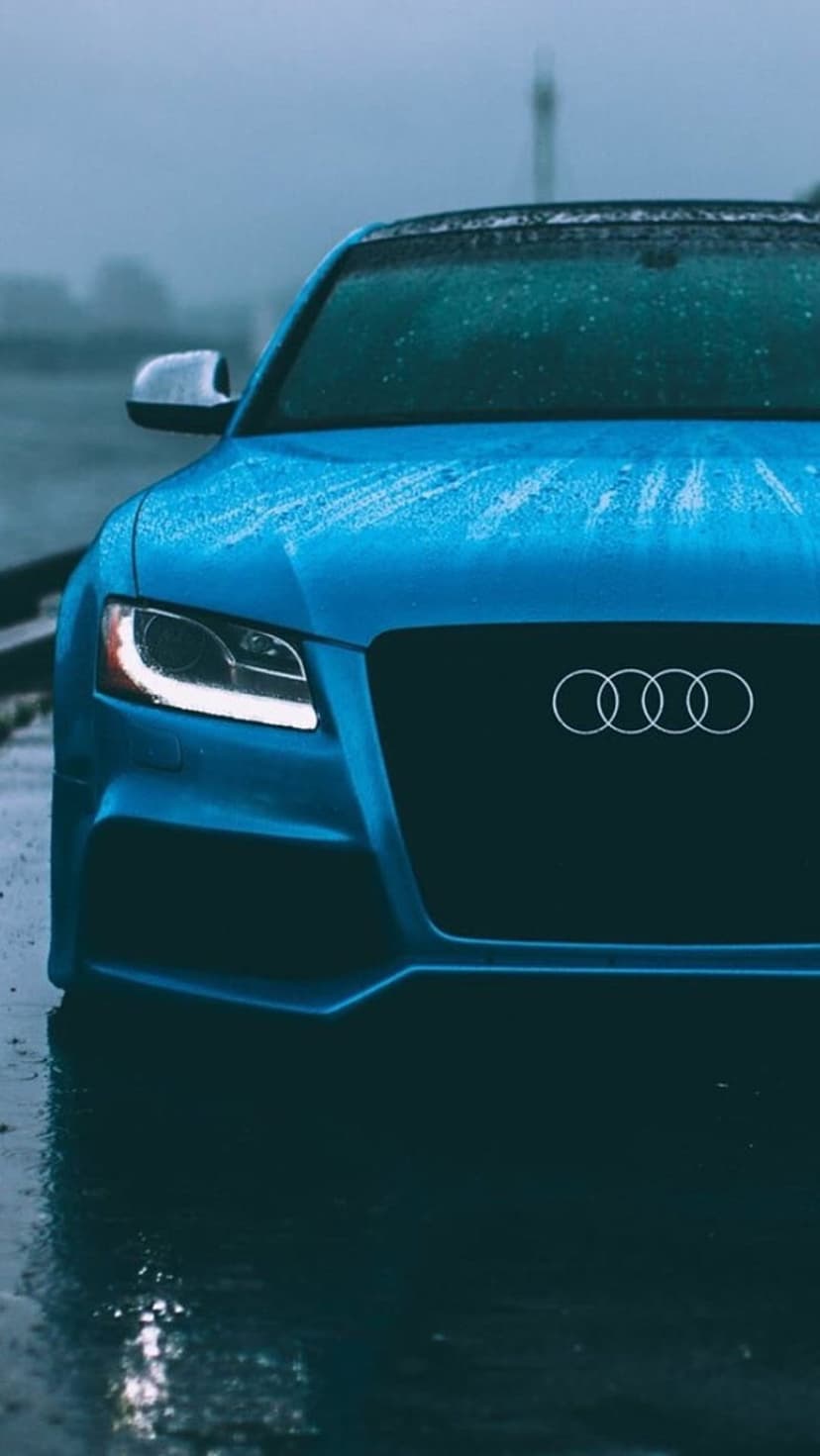 Audi S5 front grille and headlights covered in raindrops and frost on a wet road in moody winter weather.