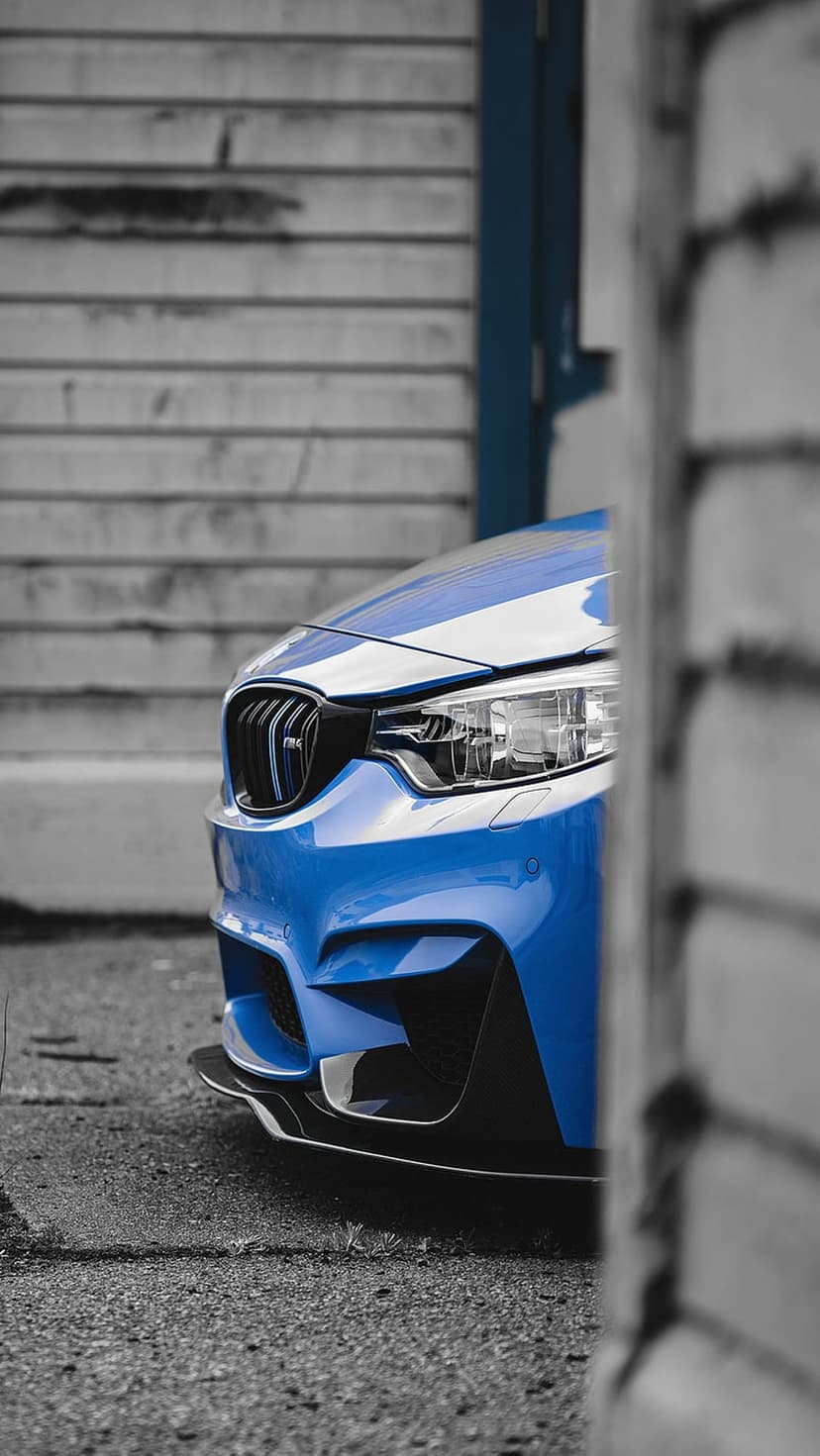 Blue BMW M4 front grille and LED headlight detail against a textured brown wooden wall in a low-angle shot.