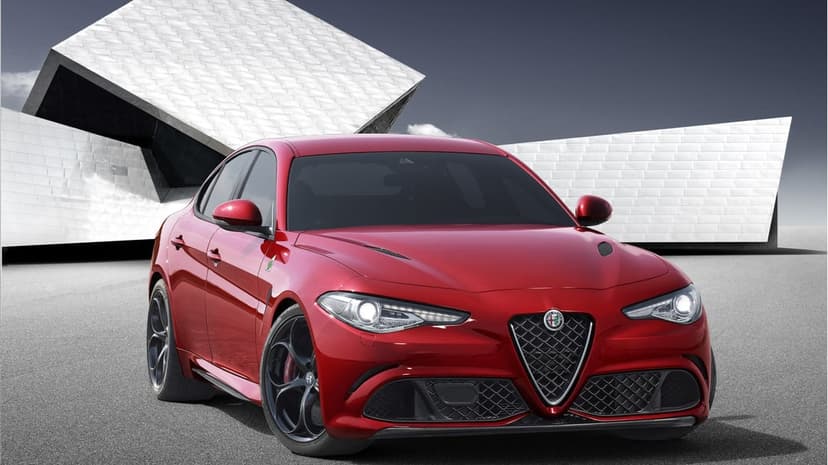 Red Alfa Romeo Giulia Quadrifoglio sports sedan parked on asphalt against a geometric white tiled building.
