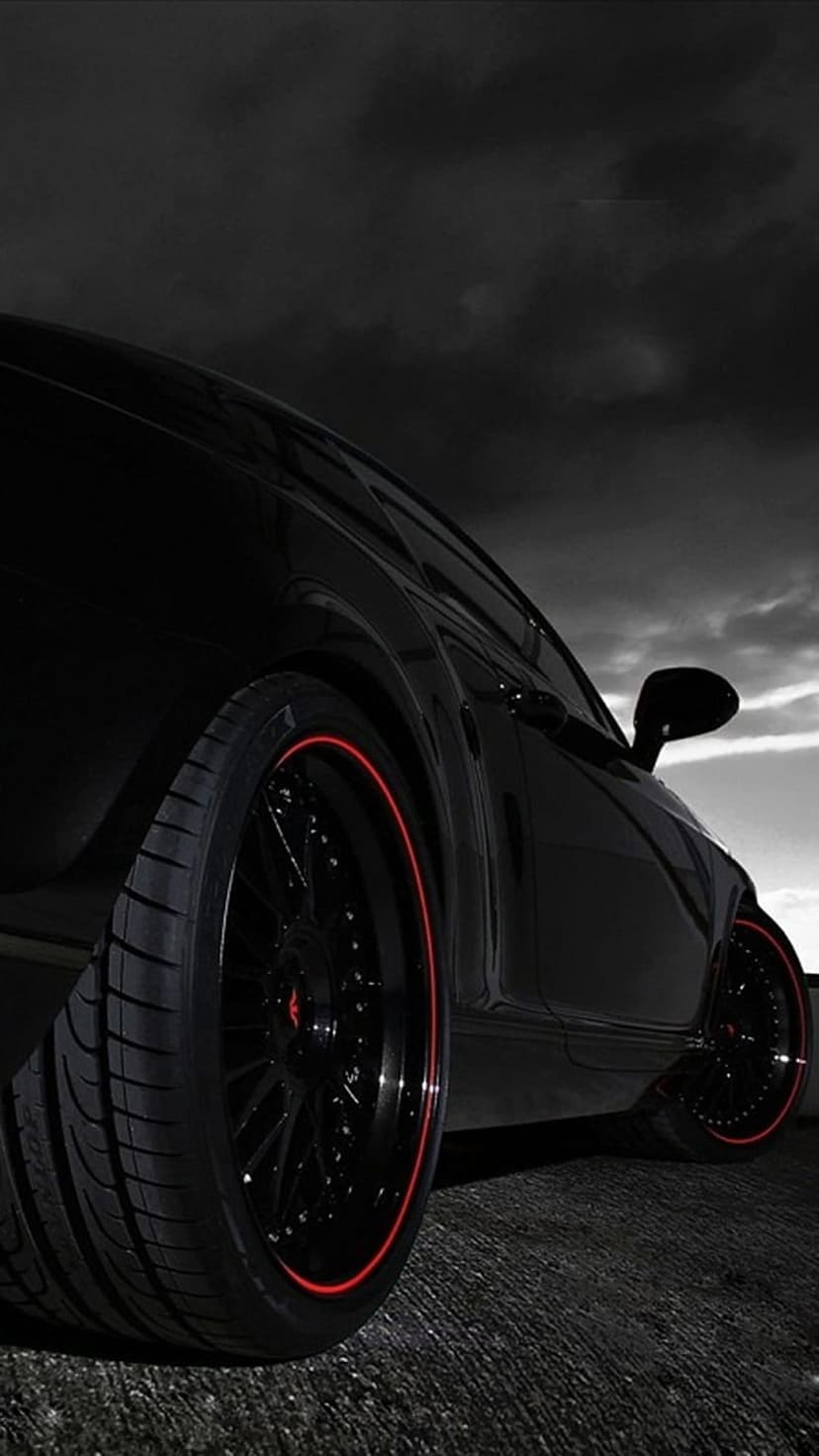 Black sports car with red-rimmed wheels rests on textured asphalt against a dramatic, cloudy grey sky.