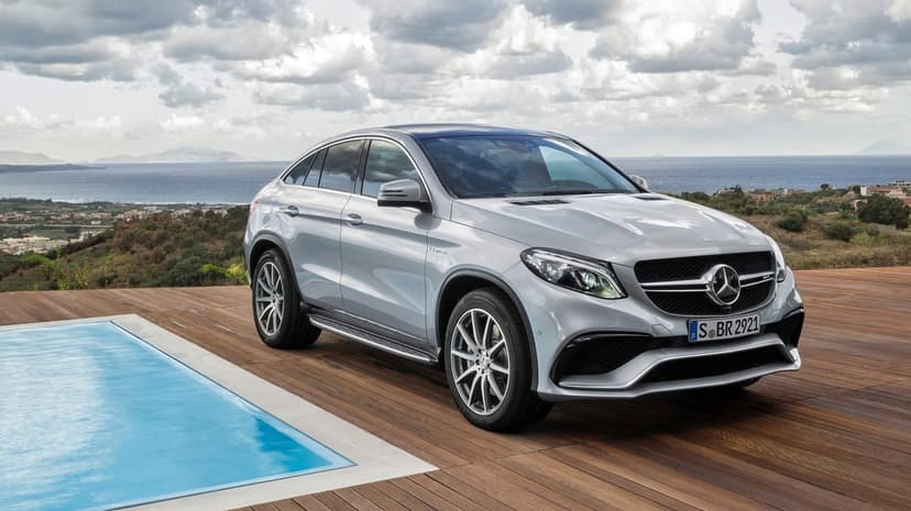 Silver Mercedes-AMG GLE Coupe parked on a wooden deck by a pool with a Mediterranean sea view and cloudy sky.