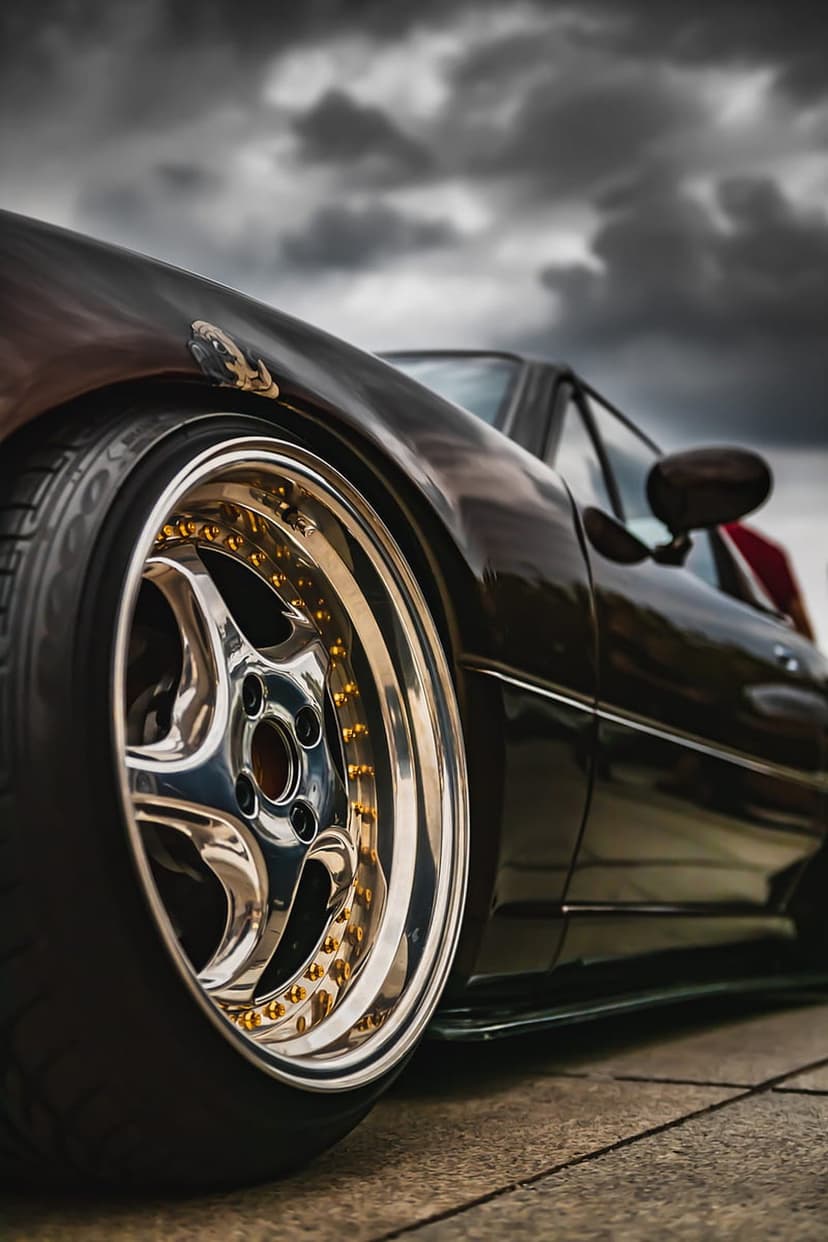 Multi-spoke gold and chrome car wheel on a dark vehicle with a low-profile tire under a moody overcast sky.