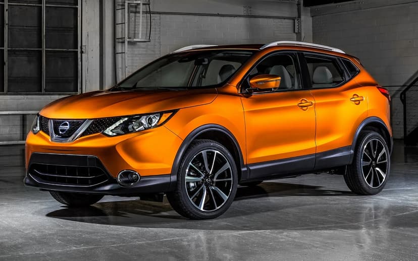 Metallic orange Nissan Rogue Sport SUV parked in an industrial warehouse with studio lighting and alloy wheels.