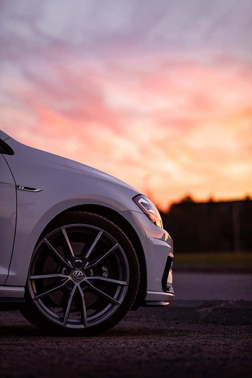 White Volkswagen Golf R front wheel and fender reflect orange sunset light during twilight in a vertical shot.