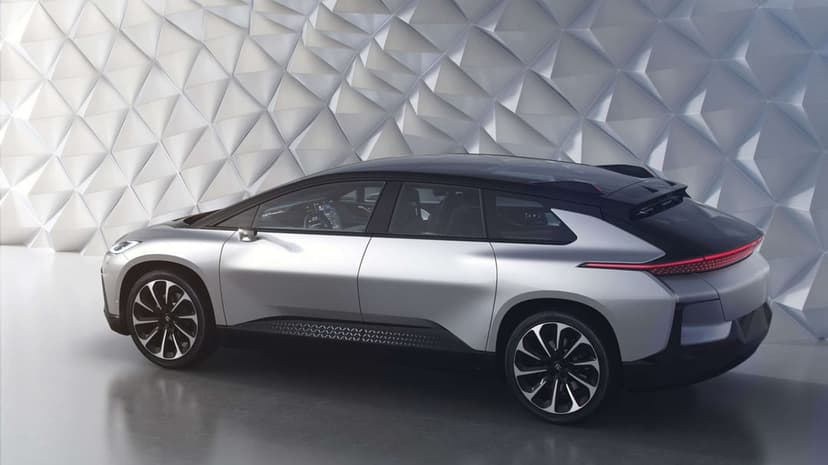 Silver futuristic electric SUV parked against a white faceted geometric wall in a bright minimalist studio.