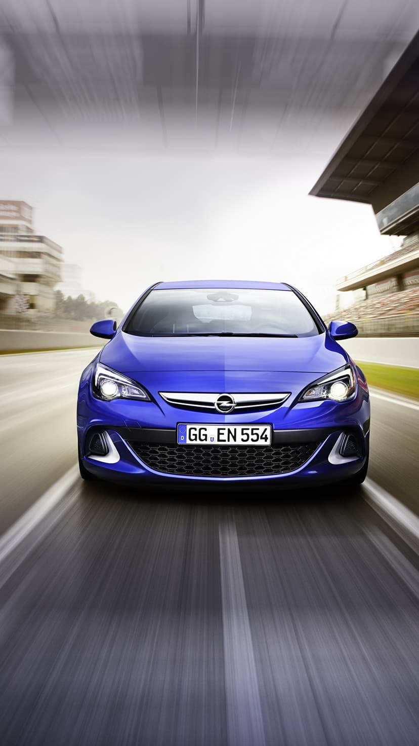Front view of a blue sports car speeding on a racetrack with intense motion blur and grandstands in the background.