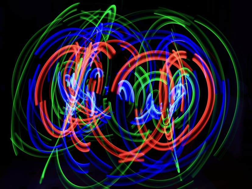 Vibrant blue, green, and red light streaks swirl in circular patterns against a dark, pitch-black background.