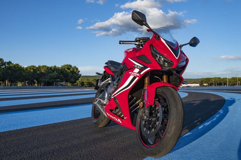 Red Honda CBR650R motorcycle on a blue and black striped racetrack under a bright blue sky with clouds.