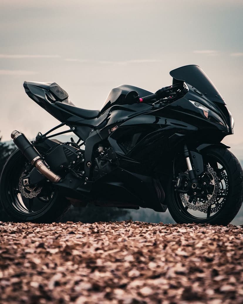 Black Kawasaki Ninja sportbike parked on wood chips against a soft overcast sky with carbon fiber exhaust.
