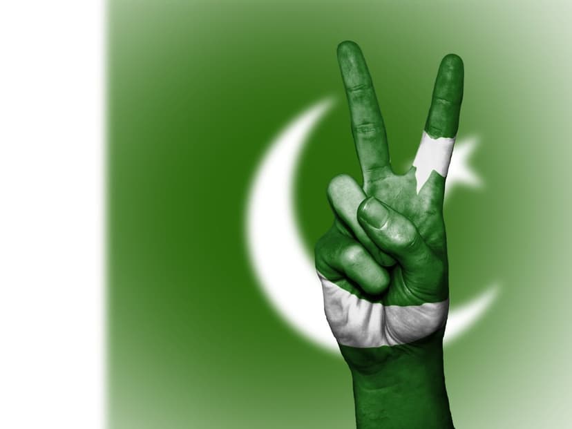 Pakistani flag painted hand makes a victory sign against a blurred national flag background in vertical view.