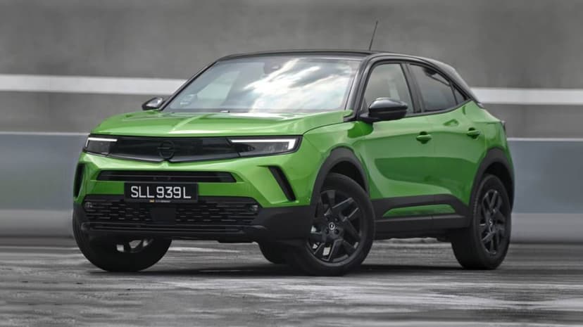 Green Opel Mokka SUV with a black roof parked on a gray concrete surface under natural daylight.