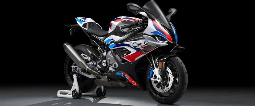 BMW M 1000 RR sportbike with white and blue livery and carbon fiber parts against a black studio background.