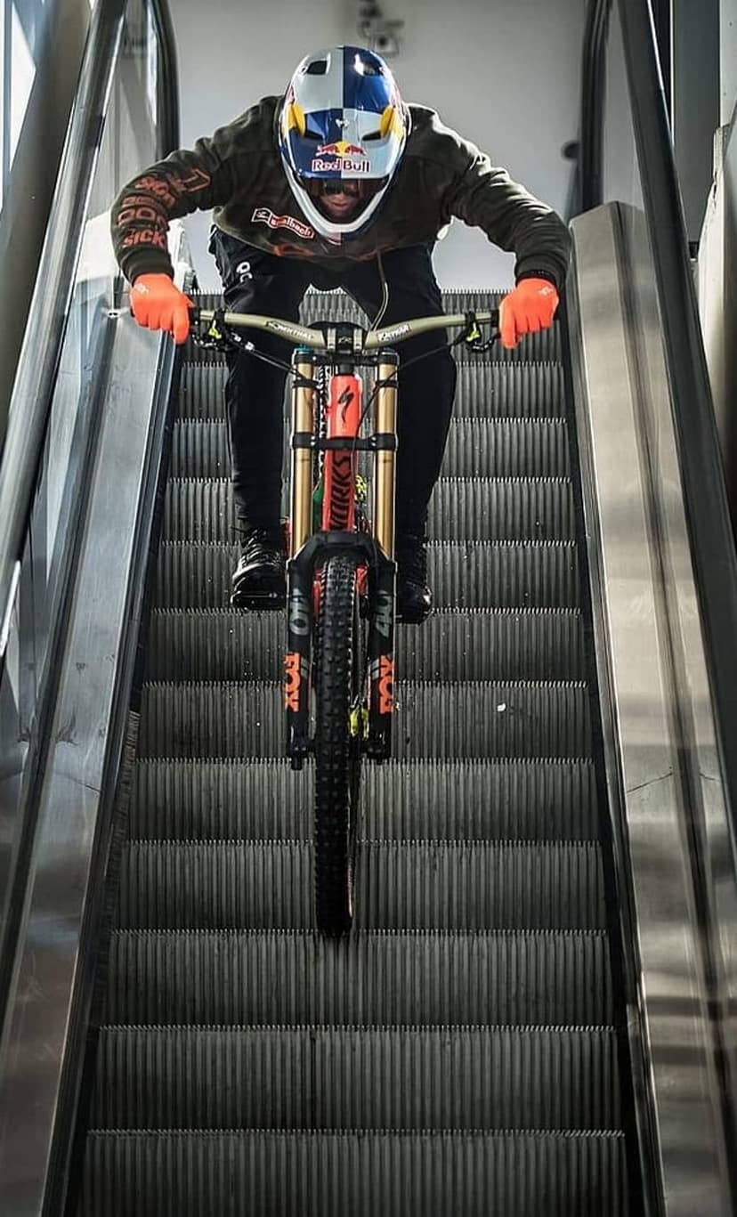 Mountain biker in orange gloves and a helmet rides a full-suspension bike down a metallic escalator.