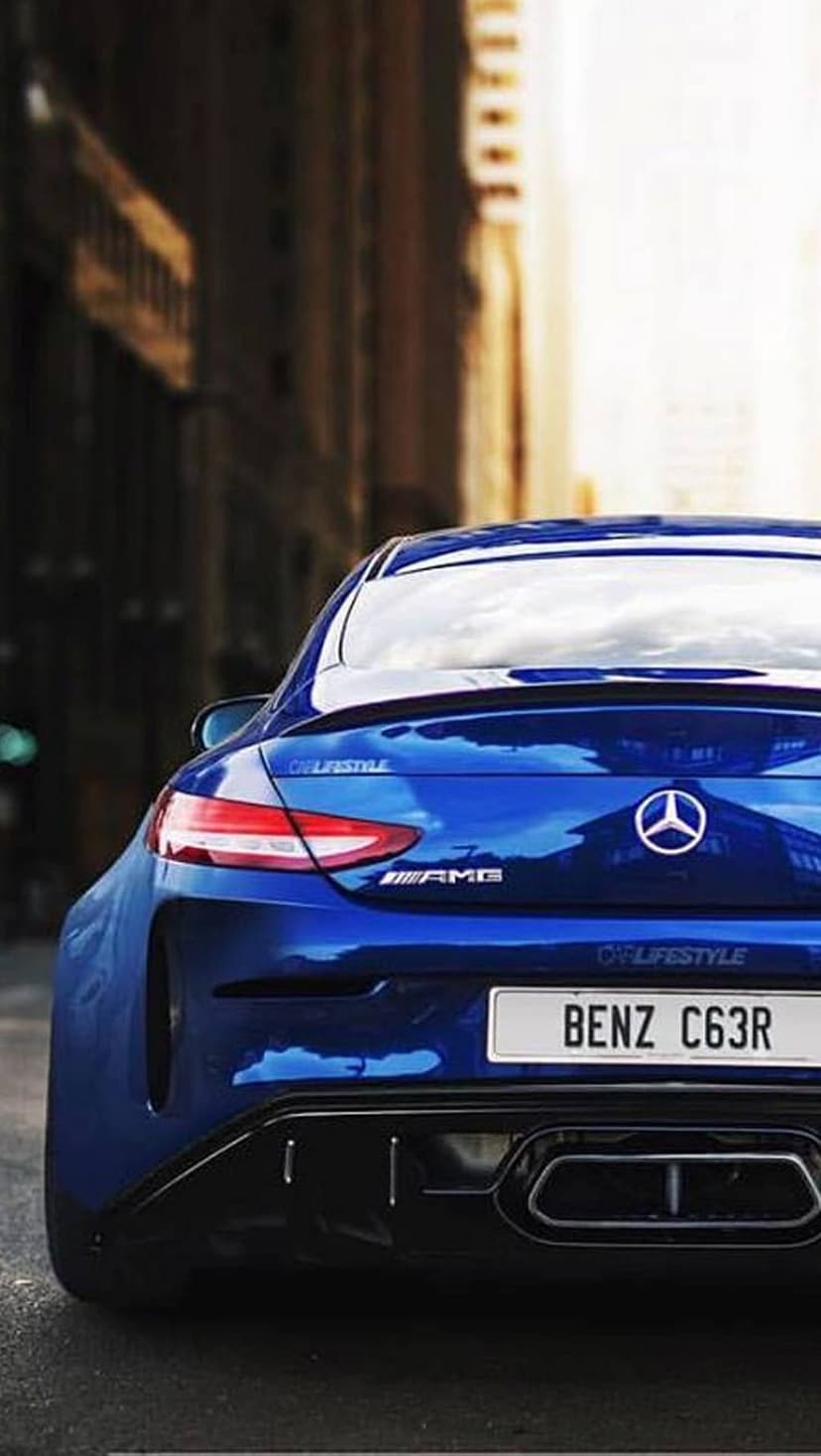 Mercedes-AMG C63R Coupe with metallic blue paint and quad exhausts parked on a blurred urban street at dusk.