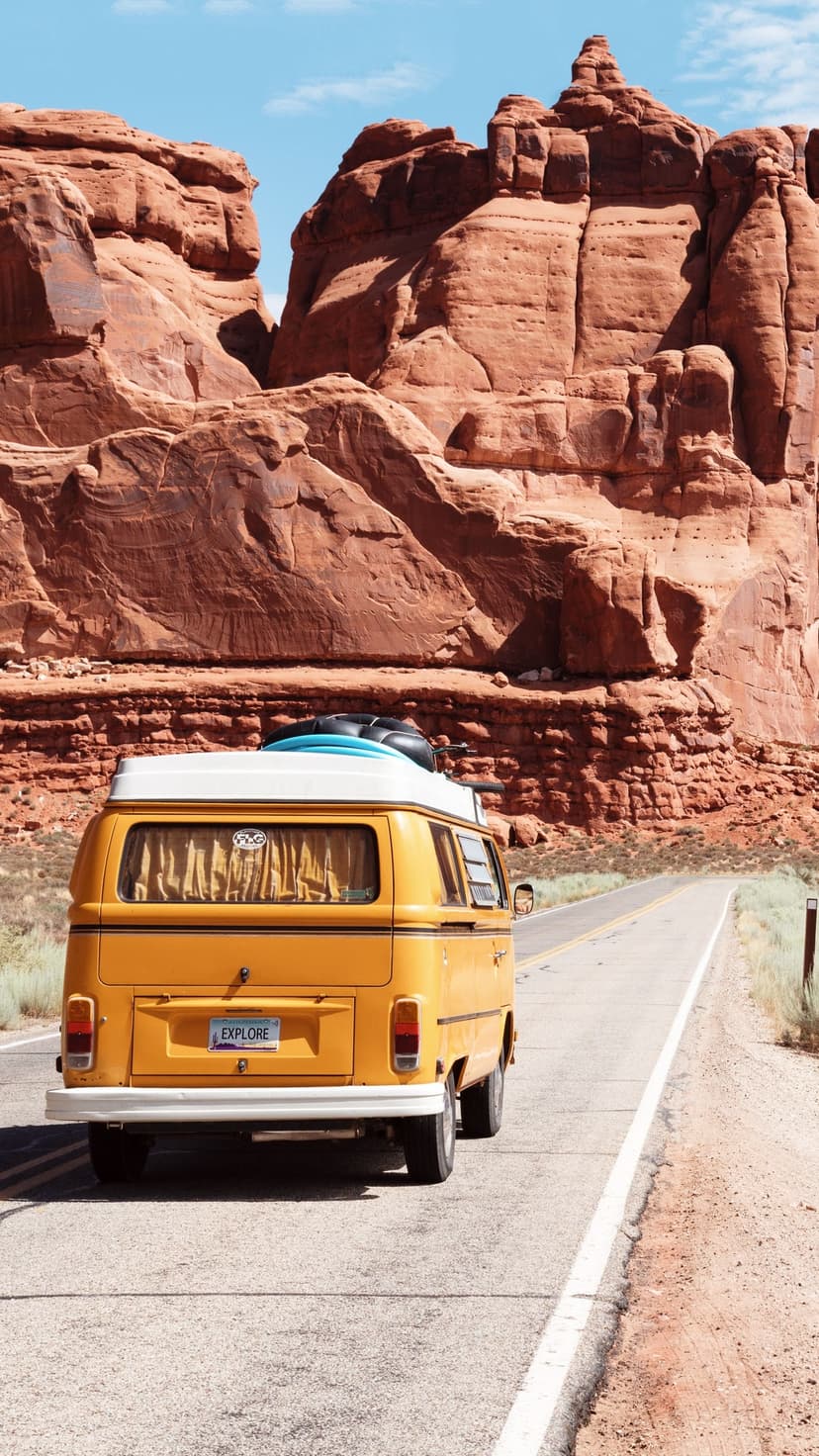 Yellow vintage van with surfboards on a desert road between red rock formations in Arches National Park.