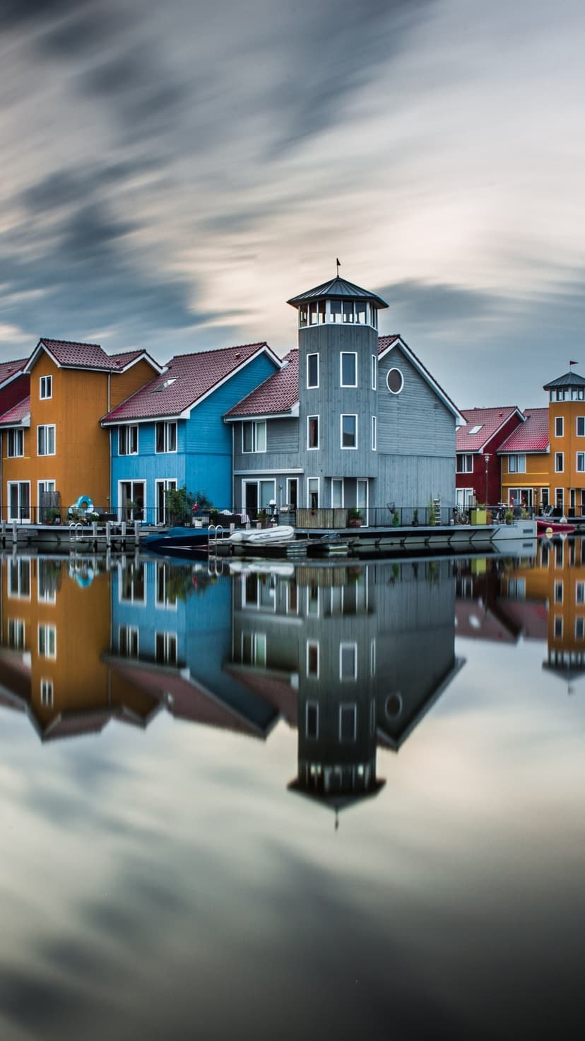 Brightly painted row houses reflected in a still canal with small boats moored along the water's edge.